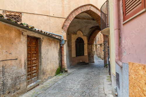 Fototapeta Naklejka Na Ścianę i Meble -  Italy, Sicily, Palermo Province, Castelbuono. Archway over cobblestone street in the town of Castelbuono.