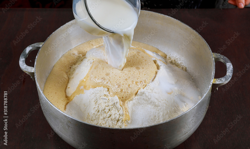 Pouring milk on yeast dough for making bread.