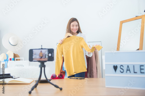 Beautiful asian woman blogger showing clothes in front of camera to recording vlog video live streaming at her shop.Business online influencer on social media concept.