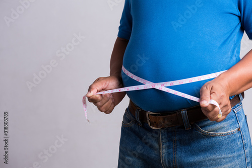 Foto Overweight or fat adult man in very tight jeans with measuring tape on a gray background