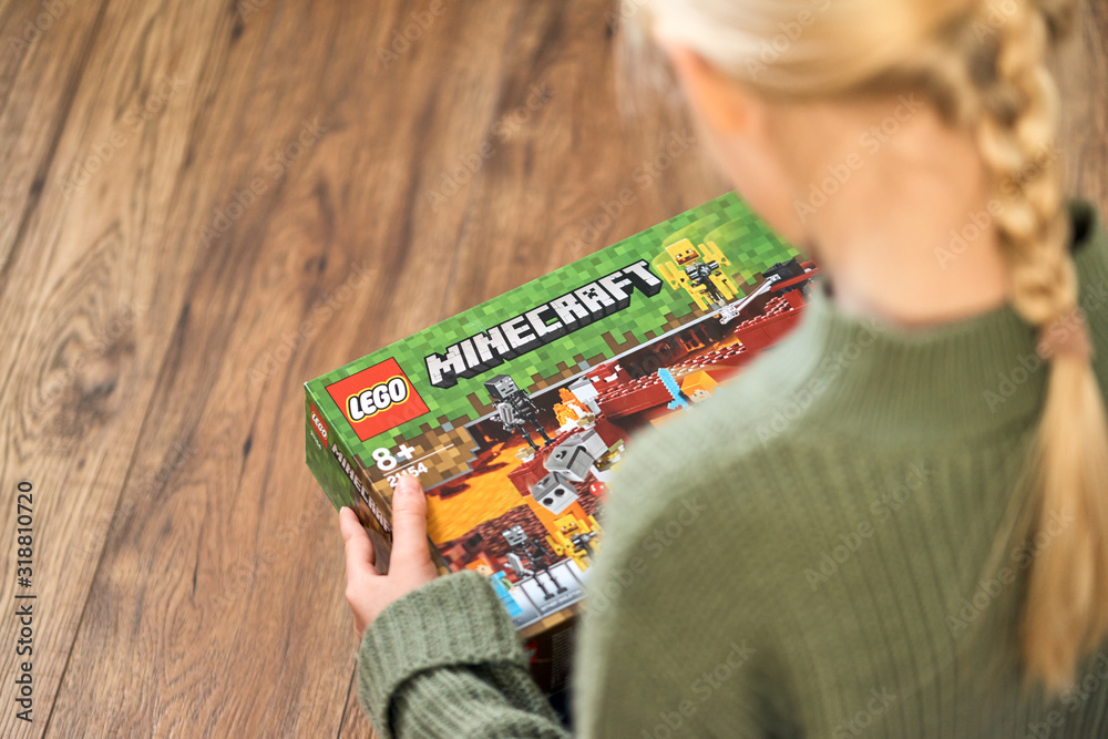 Naklejka premium January 5, 2020, Kaliningrad, Russia. A little girl with blond hair is holding a new box of Lego Minecraft and looks at it.