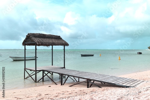 Over water thatched hut  rustic bungalow with a wooden planked walkway installed on a white sand beach.