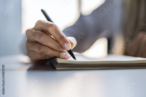 Closeup of woman hand writing in notepad on a white table. Focused on a hand with pen