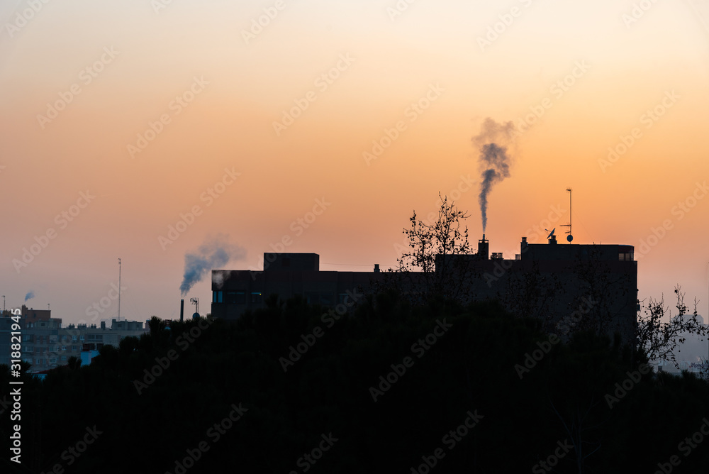 Urban landscape with the silhouette of buildings with chimneys expelling smoke at sunset