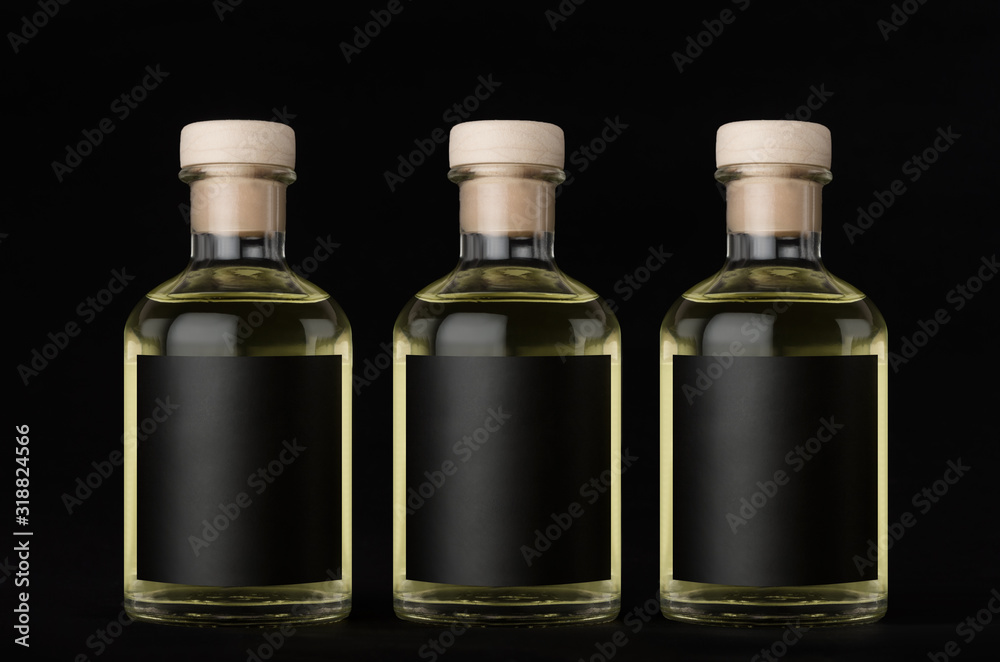 Three glass bottles for cosmetic, perfume, drink with black label, cork, yellow liquid in a row on dark black background, mock up for design of product. Three glass bottles for cosmetic, perfume, drink with black label, cork, yellow liquid in a row on dark black background, mock up for design of product.