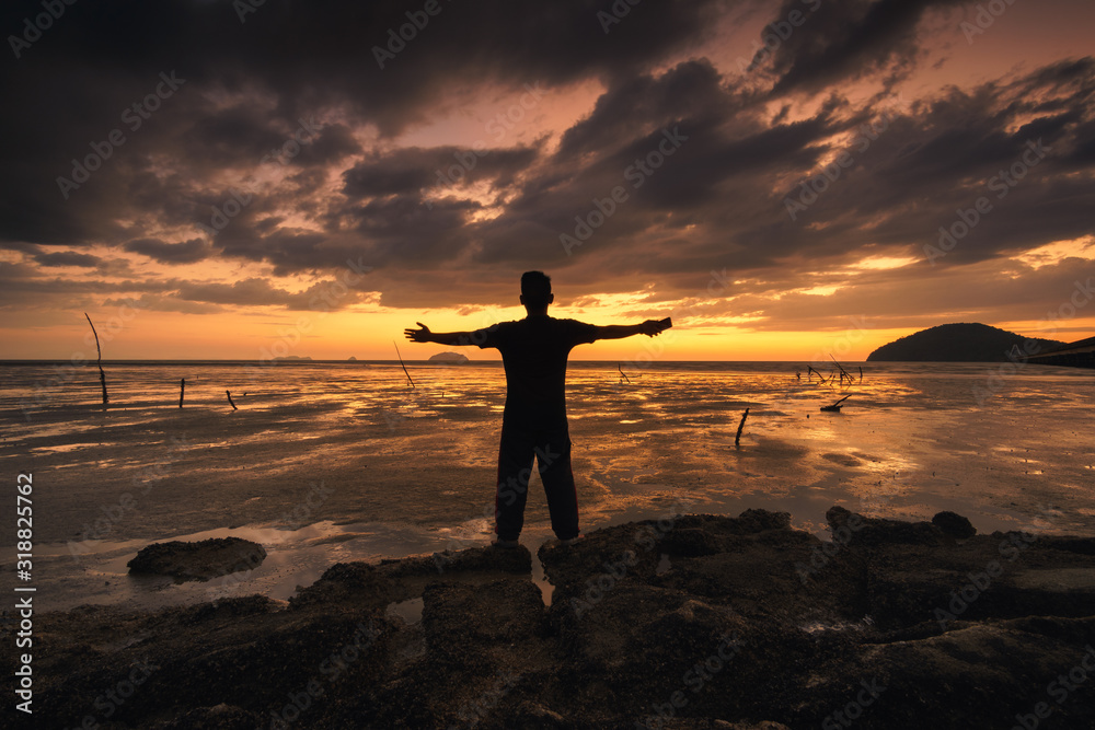 Fototapeta premium silhouette of back of a man operating his phone against beautiful sunset at beach