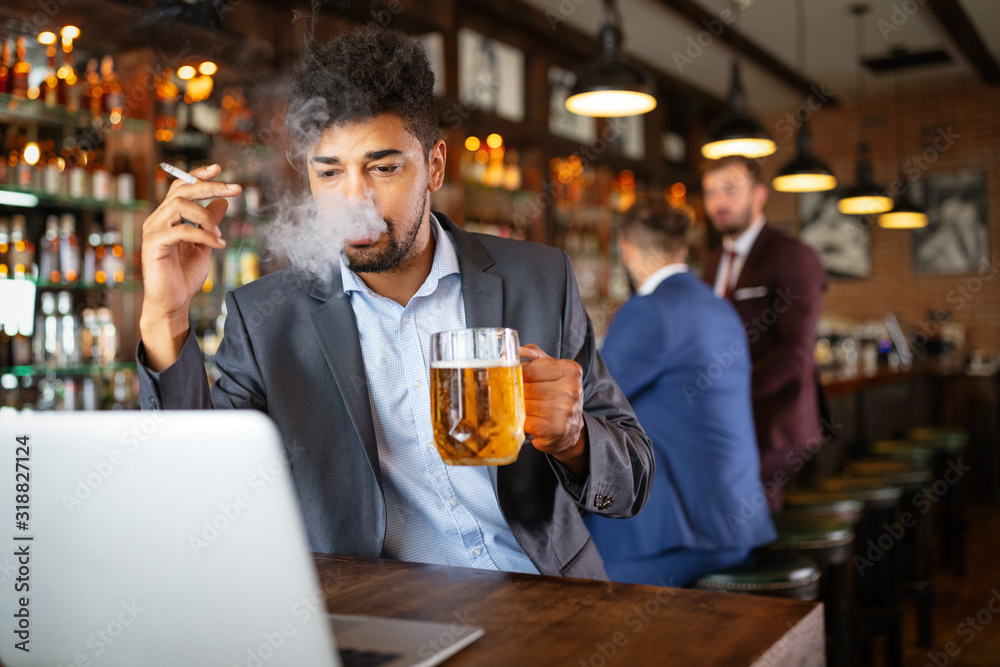 Man drinking beer and smoking cigarette while working on computer. Bad habit concept.