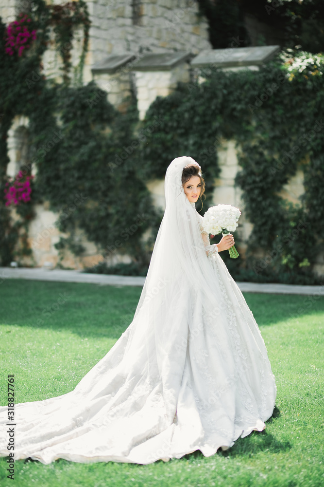 Beautiful bride in elegant white dress holding bouquet posing in park