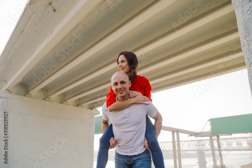 Happy girl on the back of a man at the bridge. Lovers have fun.