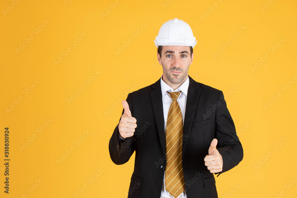 Young handsome businessman wears suit and construction helmet on isolated yellow background. Young handsome businessman wears suit and construction helmet on isolated yellow background.