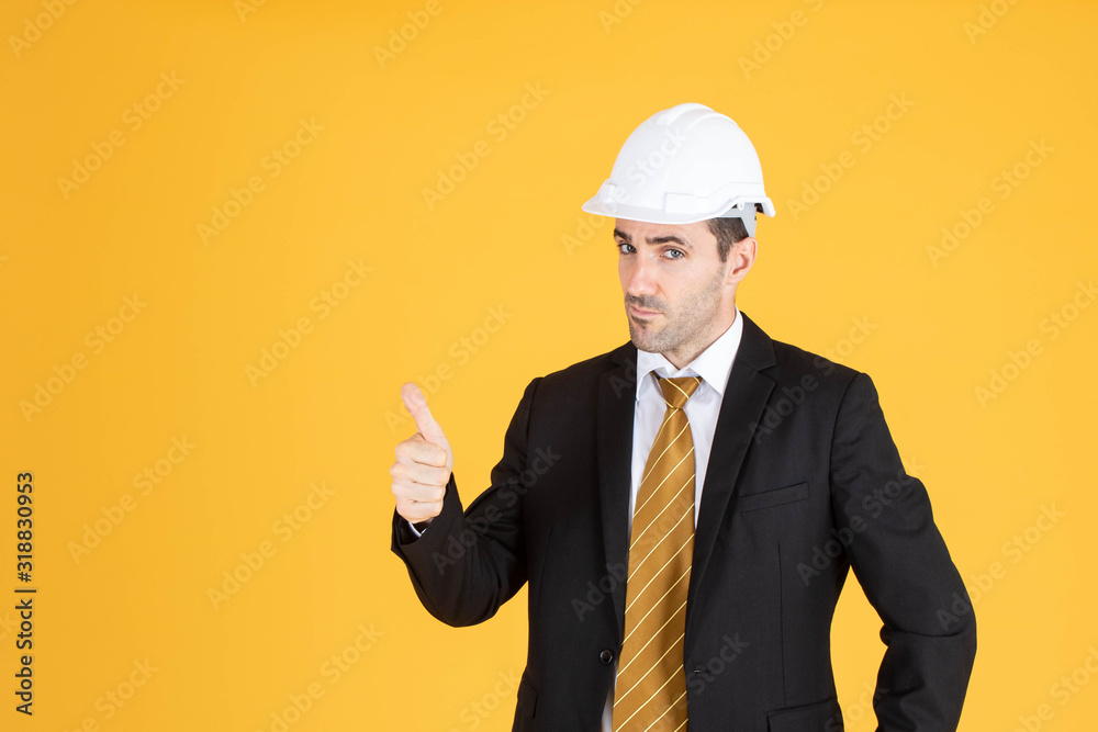 Young handsome businessman wears suit and construction helmet on isolated yellow background. Young handsome businessman wears suit and construction helmet on isolated yellow background.