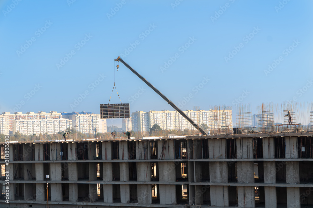 Construction of a multistorey monolithic residential complex, with workers. A mounting crane carries a large concrete slab