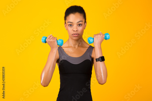 Black Girl Doing Dumbbell Bicep Curls Pumping Muscles, Yellow Background