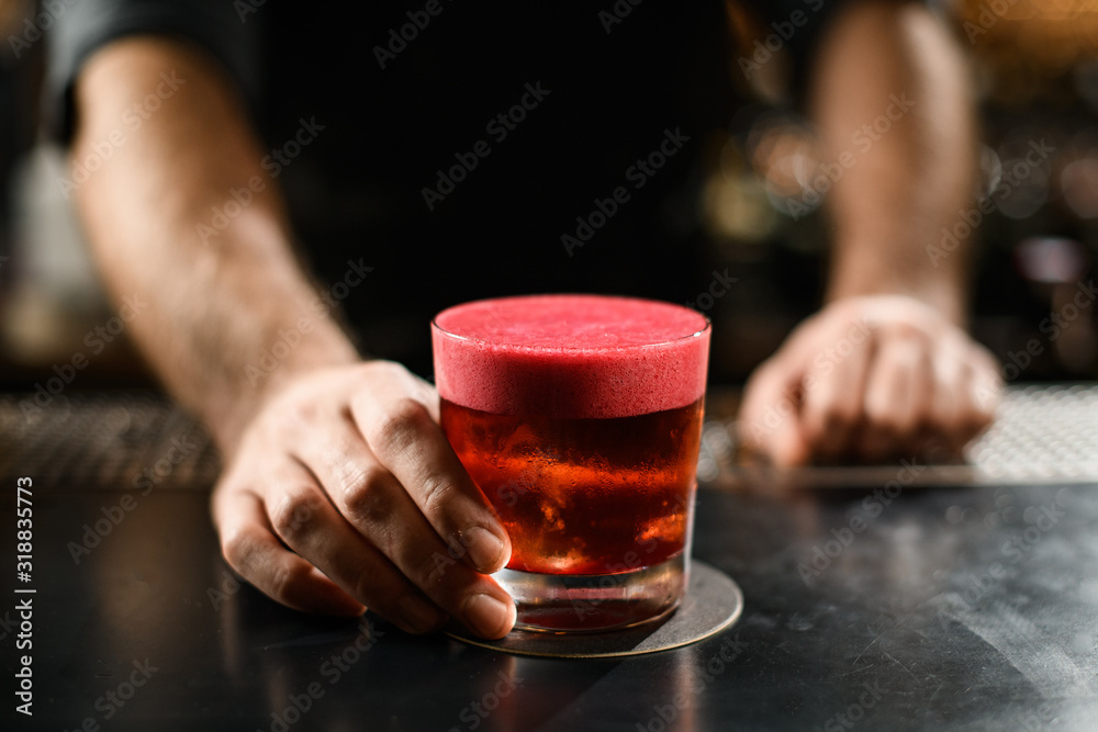 Male bartender serving the golden brown cocktail in the glass decorated with a smooth pink scum Male bartender serving the golden brown cocktail in the glass decorated with a smooth pink scum