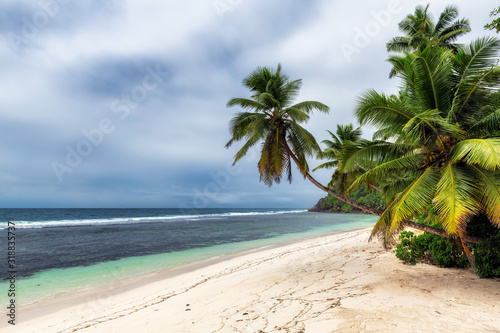 Tropical raining whether on the sandy beach with coconut palm trees and tropical ocean in paradise islands Seychelles.