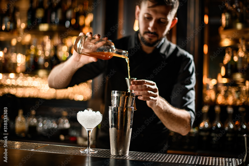 Male bartender pouring an orange alcoholic drink from the bottle to a steel jigger