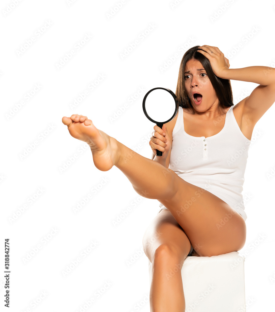 Young shocked woman looking her leg through the magnifying glass Young shocked woman looking her leg through the magnifying glass