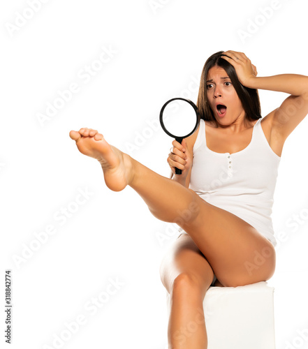 Young shocked woman looking her leg through the magnifying glass
