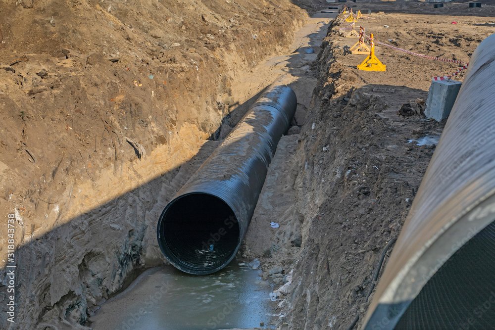 black plastic pipes are in trench of ground. process of laying of