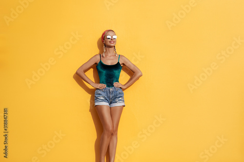 Summer urban fashion. Fun and colorful. Young pretty happy woman in shorts posing against yellow wall.