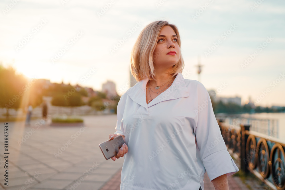 Attractive young woman using smartphone while walking down the city promenade.