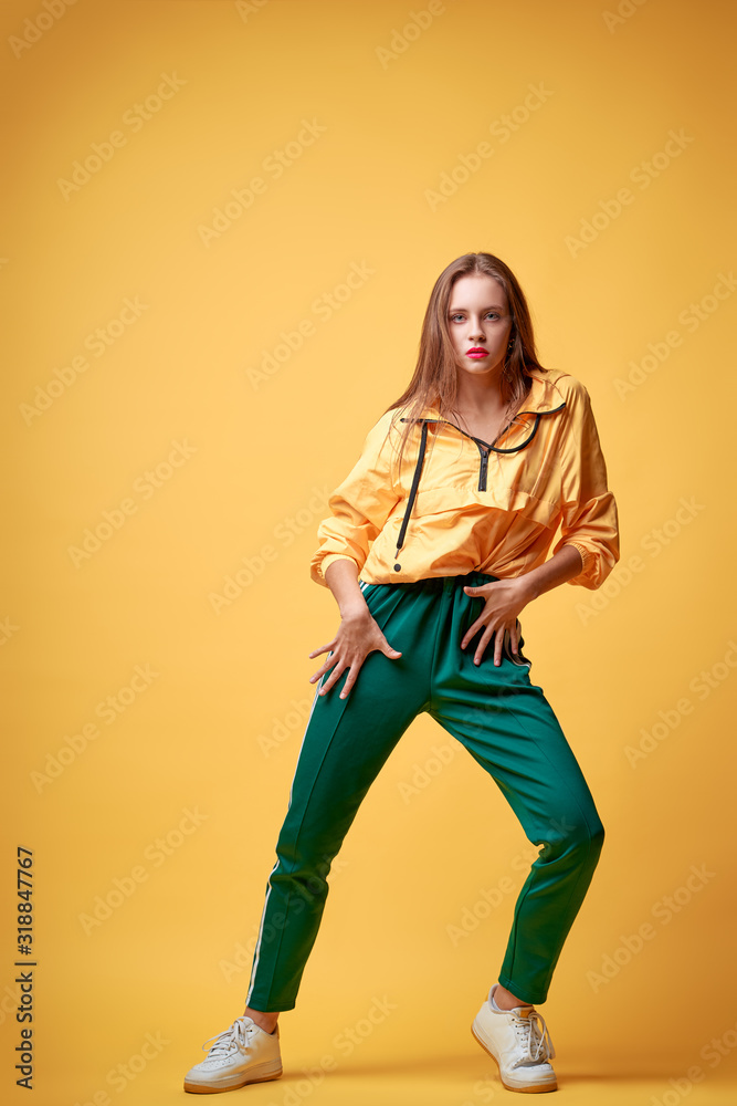 Colorful studio portrait of happy young girl dancing against yellow background.