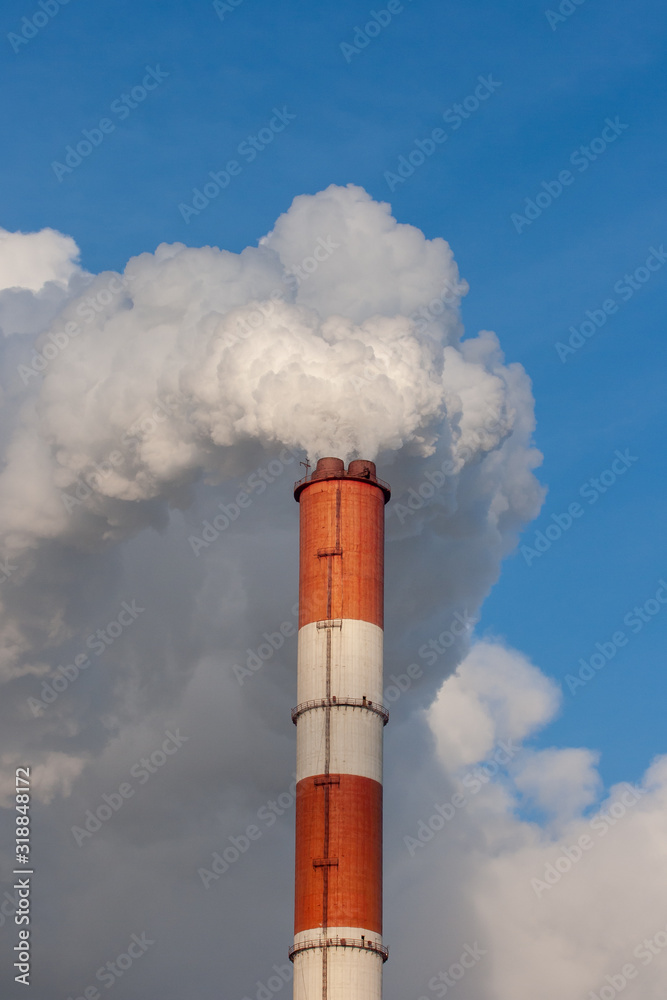 Clouds of smoke ascend from the pipes of an industrial enterprise against a blue sky Clouds of smoke ascend from the pipes of an industrial enterprise against a blue sky