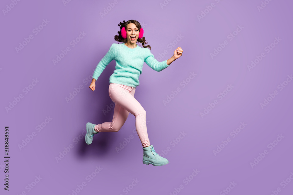 Full length photo of funky lady jumping high up excited good mood rushing sale sopping center wear fuzzy pullover pastel pink ear muffs pants shoes isolated purple color background