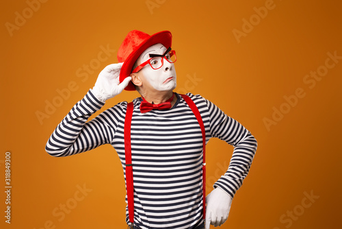 Listening mime red hat and striped t-shirt on blank orange background