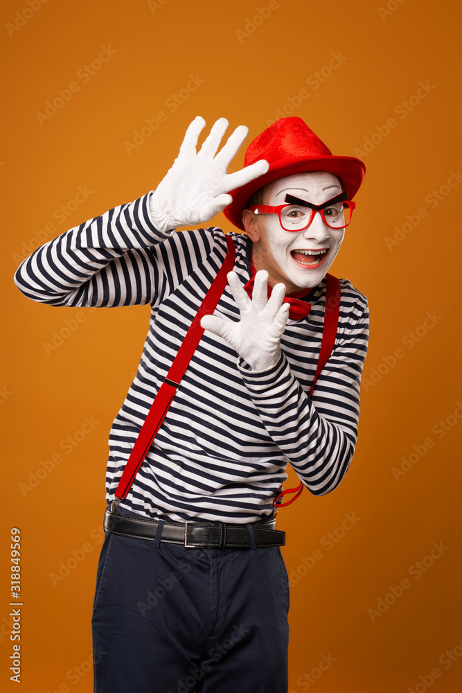 Happy mime with white face in red hat and striped t-shirt on blank orange background