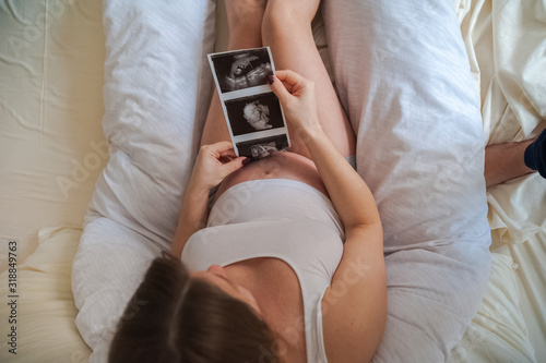 Pregnant woman with ultrasound picture of baby closeup. Snapshot of ultrasound and stomach. Pregnant on a pillow for pregnant women and copy space.