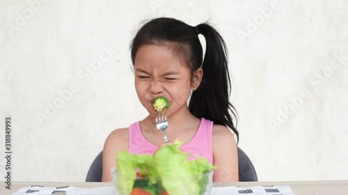 little asian girl do not want to eat vegetables and dislike taste of broccoli,spinach,tomato. the girl resolutely repels the vegetables with her hand. healthy food concept.