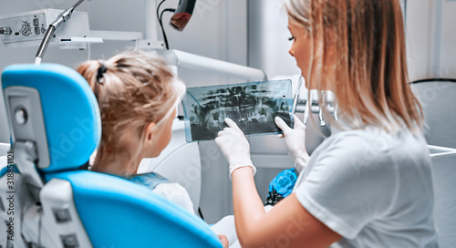 Patient at dentist office. Cheerful little girl sitting at the chair in dental office while doctor showing something at X-ray photo