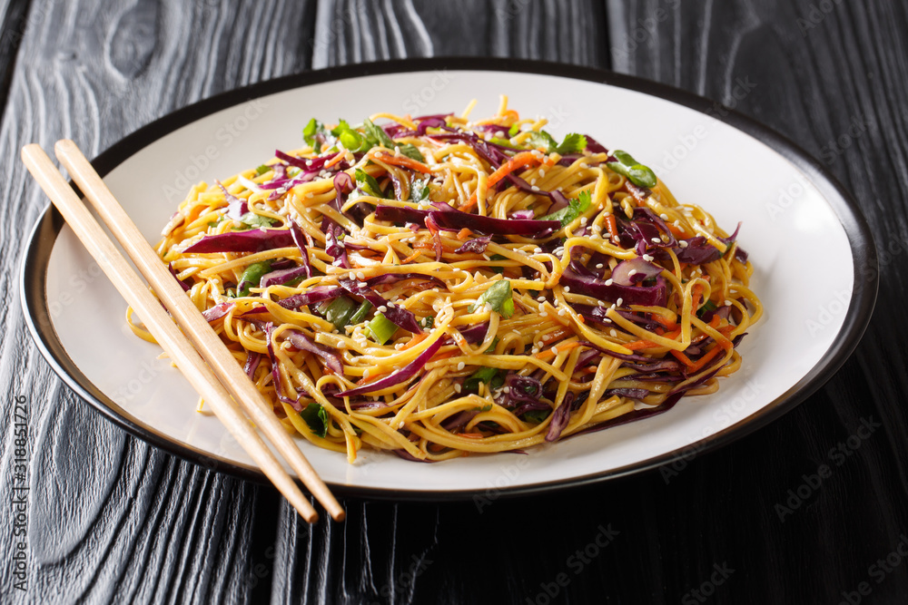 Serving egg noodles with red cabbage, carrots, green onions, green beans and sesame seeds close-up on the table. horizontal