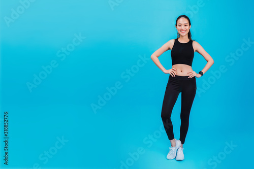 Portrait of confident beautiful asian fitness woman standing after exercise isolated on blue color background with copy space.Concept of slim and healthy happy girl workout.