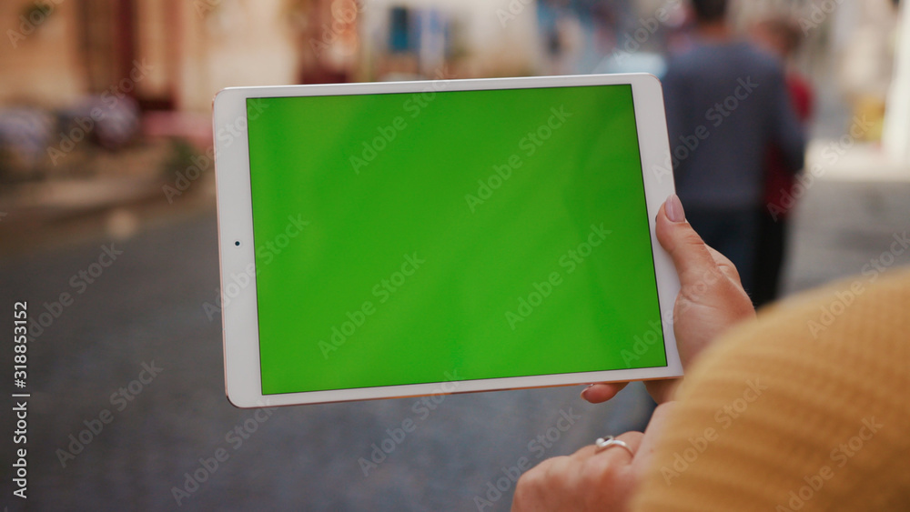 Woman showing horizontal greenscreen of mock-up tablet computer standing on the street with modern device close-up. Woman showing horizontal greenscreen of mock-up tablet computer standing on the street with modern device close-up.