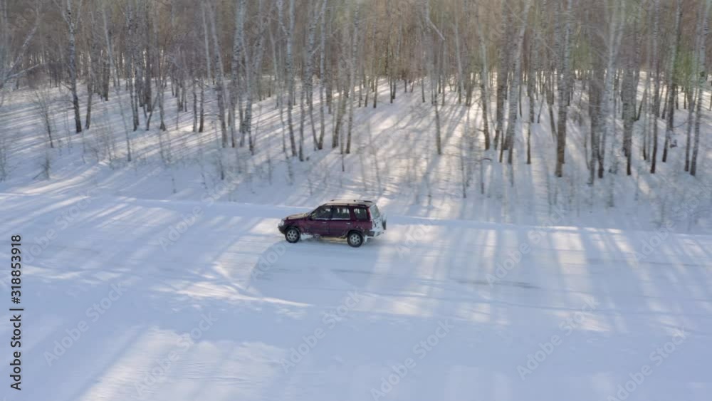 Aerial shot tracking. Modern car moves fast along snowy forest road in rural areas Aerial shot tracking. Modern car moves fast along snowy forest road in rural areas