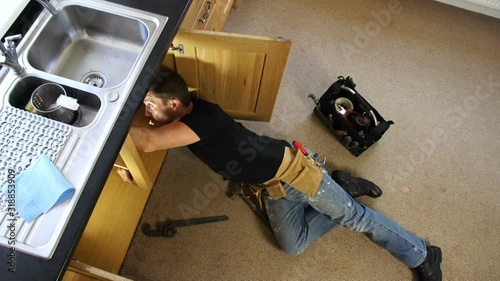 Plumber / Handyman fixing a leak. The tradesman is lying down under the sink to repair the pipe. Pan shot.