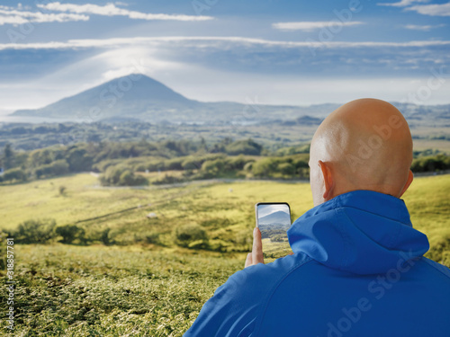 Male tourist taking picture on his smart phone of mountain landscape, Selective focus, Concept travel, capture and share experience with help of modern technology.
