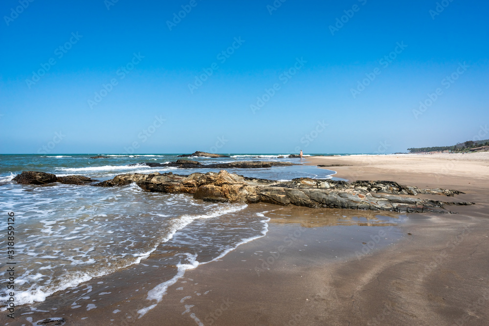 Long sandy beach background. Panoramic view of the Arabian sea coast in India. Large boulders on the shore. Surf Waves breaking on the stones. Horizon line of the ocean. Long sandy beach background. Panoramic view of the Arabian sea coast in India. Large boulders on the shore. Surf Waves breaking on the stones. Horizon line of the ocean.