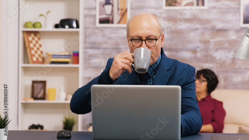 Old man enjoying a cup of coffee while working on laptop