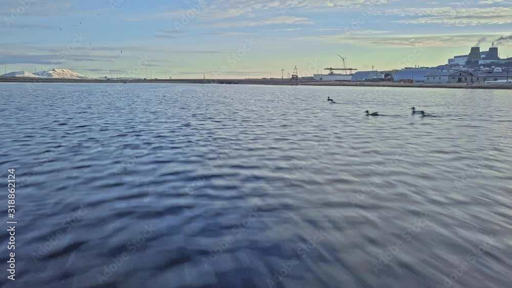 pictorial city with factory on river bank against hill covered with snow under cloudy sky aerial low angle motion above water pictorial city with factory on river bank against hill covered with snow under cloudy sky aerial low angle motion above water