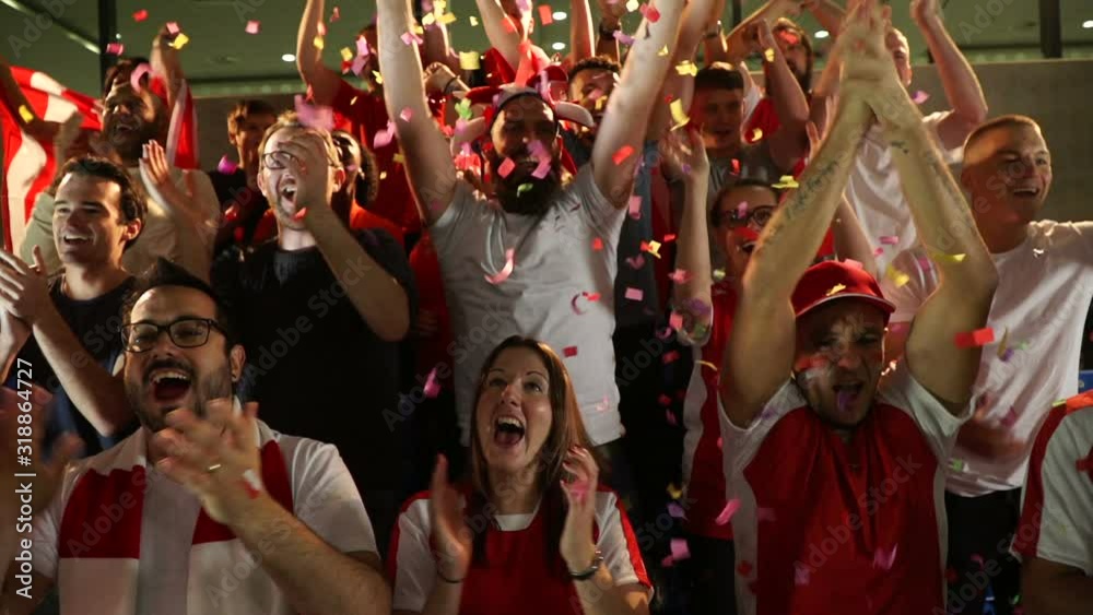 Football / Soccer fans or supporters in stadium celebrate with confetti falling. They jump and cheer. Super slow motion.