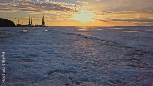 picturesque frozen river with tracked all-terrain vehicles traces reflects evening sunlight aerial low angle motion above water