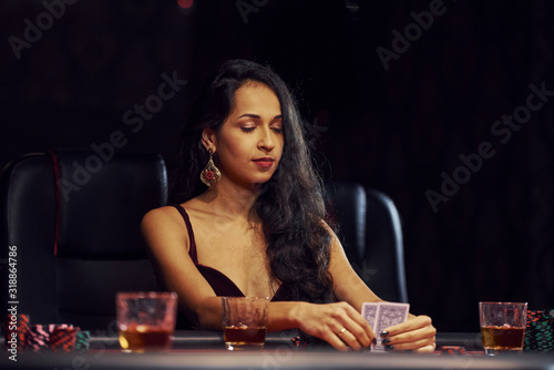 Woman in elegant clothes sits in cassino by table and plays poker game