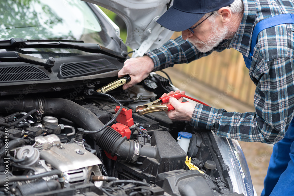 Car mechanic using car battery jumper cable Car mechanic using car battery jumper cable