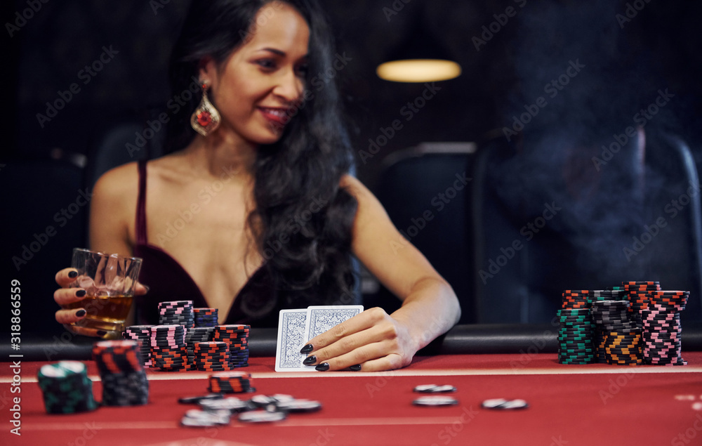 Fototapeta premium Woman in elegant clothes sits in cassino by table and plays poker game
