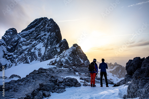 Skiers staring at the sunrise over a mountain peak.