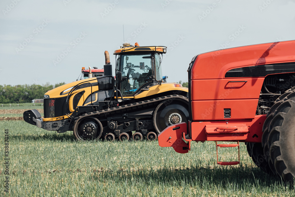 Obraz premium żółta gąsienica i czerwony traktor z dużymi kołami w polu przeciw błękitne niebo