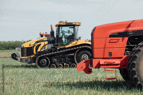 yellow caterpillar and red tractor with big wheels in the field against the blue sky